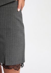 Gonna a matita grigia a righe con bordo in pizzo all'orlo. Il tessuto ha una texture liscia, con un design aderente e tasche laterali.