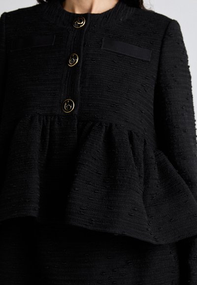 Black peplum jacket with textured fabric, featuring gold buttons and two flap pockets. The collar is round with a ribbed design.