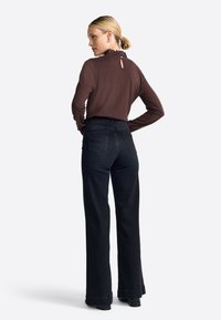 Brown long-sleeve top with ruffled collar and back keyhole detail, paired with high-waisted black wide-leg jeans with back pockets.