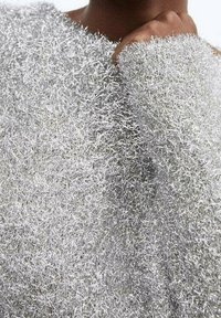 Maglione fuzzy argento con un filato metallico testurizzato. Presenta una vestibilità ampia, polsini larghi e un aspetto morbido e peloso.