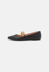 Zapato plano de cuero negro con punta afilada, que presenta un acento de cadena dorada en la parte frontal y un diseño minimalista. Textura suave.
