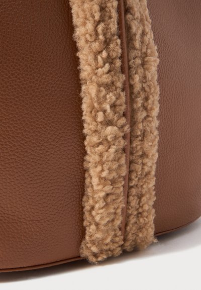 Close-up of brown textured leather with a strip of thick, curly beige shearling fabric sewn along the edge.