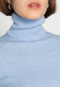 Jasnoniebieski prążkowany sweter z golfem wykonany z miękkiej dzianiny. Posiada wysoki kołnierz i bezszwowy design.