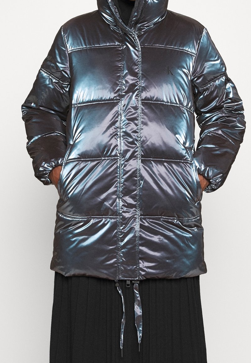 Glansig, mörk puffjacka med huva, med ett quiltat mönster, framfickor och justerbar dragsko i nederkant.