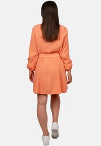 Abito arancione a maniche corte con tessuto testurizzato, vita stretta e gonna fluttuante. Abbinato a sneakers bianche per un look casual.