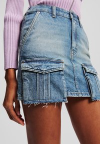 Jeans mini kjol i ljusblått, med två framfickor, fransad nederkant och en figurnära design. Materialet är texturerad, klassisk denim.