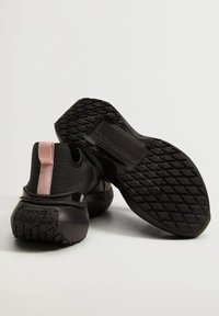 Black athletic shoes feature a textured fabric upper, pink pull tab, and a thick rubber sole with a diamond pattern for traction.