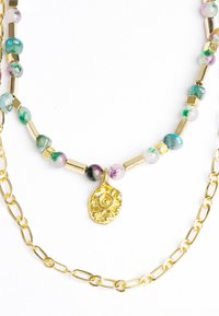 Perlenkette mit mehrfarbigen runden und zylindrischen Steinen, goldfarbigen Metallakzenten und einem goldenen Muschelanhänger.