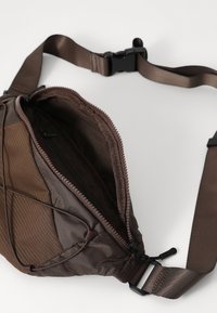 Brown fabric waist bag featuring a zippered closure, adjustable strap, and textured detailing on one side. Interior pocket visible.