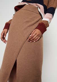 Brun stickad kjol med en sidoklyvning, med en slät textur och en åtsittande midja. Kompletterad med en flerfärgad randig tröja.