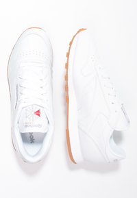 Witte leren sneakers met een laag profiel, ronde neus en vetersluiting. Beschikt over een gestructureerde zool in tan en een logo aan de zijkant.