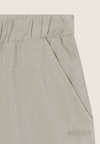 Pantaloni grigi chiari con cintura elastica, tasche laterali e un logo ricamato discreto. Tessuto morbido con una vestibilità rilassata.