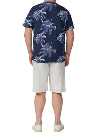 Granatowa koszulka z krótkim rękawem w białym wzorze palm, zestawiona z jasnobeżowymi szortami i białymi trampkami.