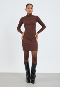 Pruun ribaga kõrge kaelusega kleit, keha lähedane disain, põlvekõrgune, sobitatud läikivate mustade põlvikontsa saapastega, sile tekstuur, minimalistlik stiil.