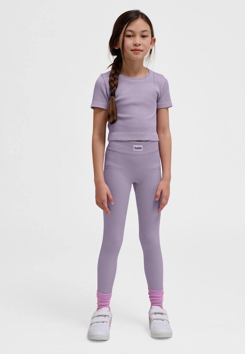 Lila geribbelde top met korte mouwen en leggings met een getailleerd ontwerp, voorzien van een merketiket op de taille en witte sneakers met klittenbandsluitingen.