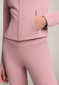 Rosa sportjacka med en åtsittande design, som har en sidoficka och matchande rosa leggings. Slät, elastisk tygtextur.