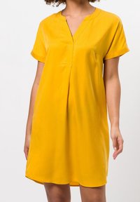 Kurzes gelbes Kleid mit V-Ausschnitt und kurzen Ärmeln. Aus glattem Stoff gefertigt, zeichnet sich durch eine lockere Passform und subtile Falten an der Vorderseite aus.