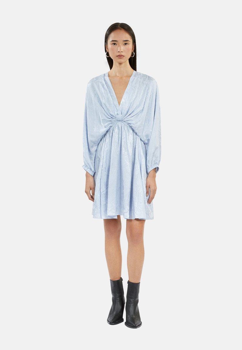 Vestido azul claro con un profundo escote en V, detalle de frente retorcido y cintura fruncida. Mangas largas y amplias, y tejido suave con una ligera textura.