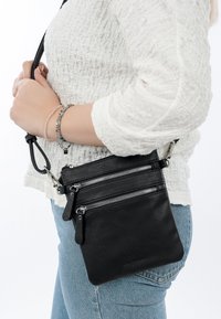 Schwarze Leder-Crossbody-Tasche mit drei gepolsterten Fächern, glatter Textur und verstellbarem Tragegurt. Robuste silberne Hardware-Akzente.