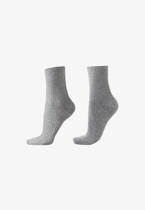 Paire de chaussettes grises côtelées mi-mollet présentées côte à côte, mettant en valeur la texture et l'ajustement à la cheville sur un fond blanc.