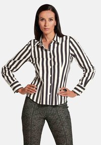 Zwart-wit gestreepte button-up shirt met een kraag, lange mouwen en een gebogen zoom. Gedragen met een patroon van donkere broek.