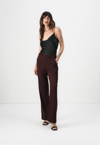 Schwarzes Satin-Camisole mit dünnen Trägern, kombiniert mit bordeauxroten, hoch taillierten Hosen. Die Hosen haben einen geraden Schnitt und seitliche Taschen.