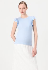 Haut à manches courtes côtelé bleu clair avec des accentuations en volants aux épaules. Associé à une jupe blanche arborant des motifs en œillets. Design simple et ajusté.