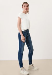 Witte T-shirt met korte mouwen, blauwe slim-fit jeans en beige high-top sneakers. Gladde stof, slim-fit vorm en contrasterend sneak ontwerp.