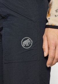 Melnas āra bikses no viegla auduma, ar sānu kabatu, kurā ir pelēks mamuta logo. Virsma izskatās gluda, ar pārdomātu šuvju izpildi.