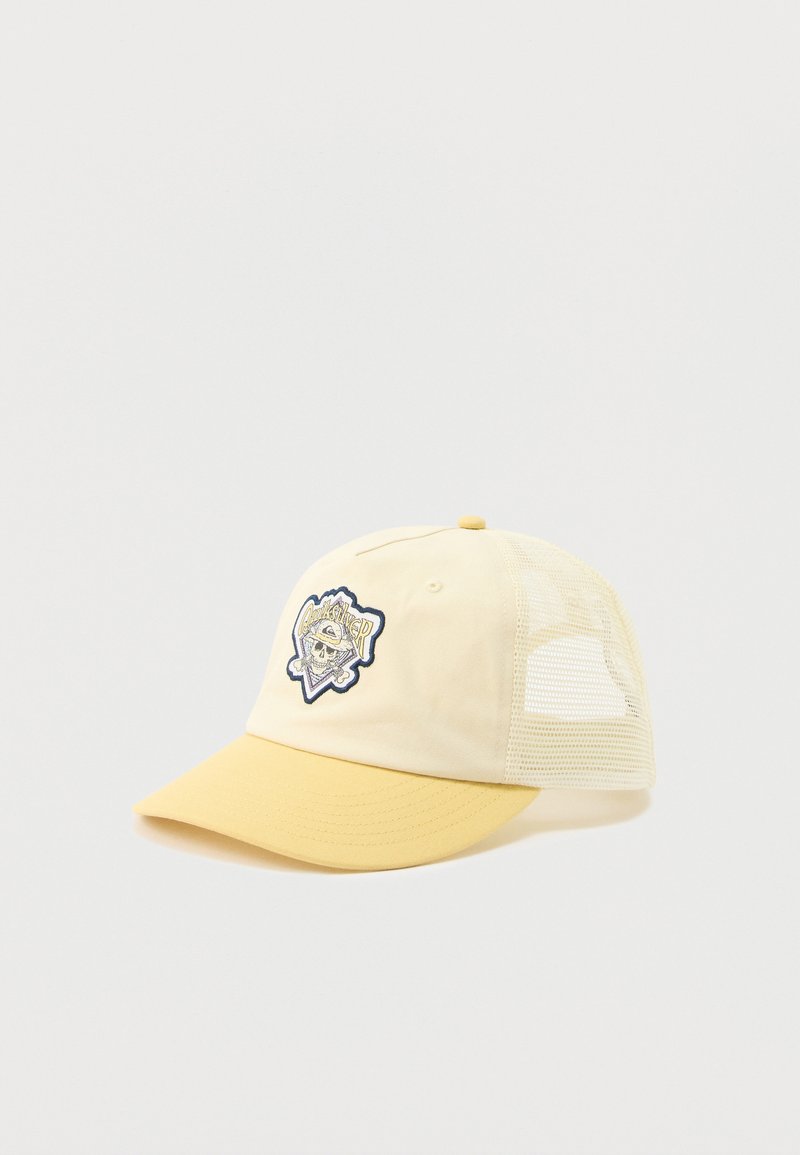 Κίτρινο και κρεμ καπέλο τύπου τρακτέρ με πλέγμα στο πίσω μέρος και κεντημένο μπάλωμα με λογότυπο κρανίου που απεικονίζει σταυρωμένα μπαστούνια μπέιζμπολ στο μπροστινό μέρος.