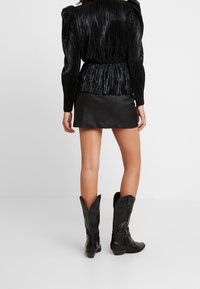 Svart plisserad långärmad topp med cinchad midja, kombinerad med en svart läder mini-kjol och knähöga svarta cowboystövlar.