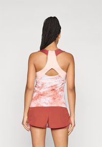 Top de desporto com alças em rosa claro e um bloco de cor em vermelho-tijolo. Apresenta um detalhe recortado nas costas e um padrão abstrato na parte inferior.