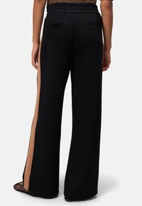 Pantalons larges noirs avec une taille texturée, dotés de panneaux latéraux beiges et de poches arrière ; tissu lisse avec un design fluide.