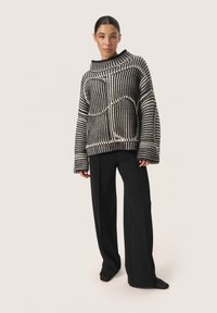 Gestreifter Oversized-Pullover in Schwarz-Weiß mit hohem Kragen und weiten Ärmeln. Kombiniert mit schwarzen maßgeschneiderten Hosen, die einen lässigen Sitz und Schnitt betonen.