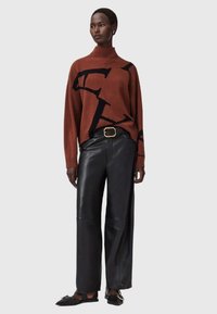 Sweter w kolorze rdzy z dzianiny o wysokim kołnierzu, z czarnymi literowymi grafikami. Szerokie spodnie z czarnej skóry o gładkiej fakturze i dopasowanej talii.