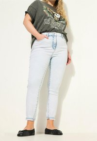 Světle modré džíny s vysokým pasem a vybledlou texturou, s knoflíkovým zapínáním a bočními kapsami, doplněné tmavým grafickým tričkem a černými balerínkami.