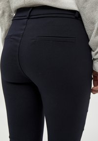 Pantaloni navy scuri su misura con una vestibilità slim, caratterizzati da una texture liscia, tasche posteriori e una vita a media altezza.