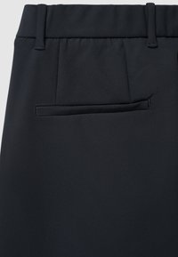 Schwarze Hose mit glatter Textur, mit flacher Vorderseite und einer Paspeltasche auf der Rückseite. Maßgeschneidertes Design mit Gürtelschlaufen.