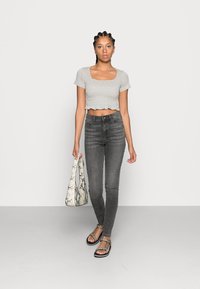 Gray cropped top with a square neckline, high-waisted dark jeans, and a snakeskin print shoulder bag. Strappy sandals with metallic accents.