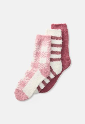 Drie paar gezellige sokken: één in roze ruitjes, één wit met roze strepen en één effen bordeauxrood; allemaal met een zachte, pluizige textuur.