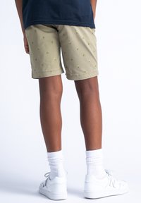 Pantaloni corti color khaki con motivo di palme verdi, tessuto misto cotone, vestibilità rilassata, indossati con sneakers bianche e calzini bianchi a coste.