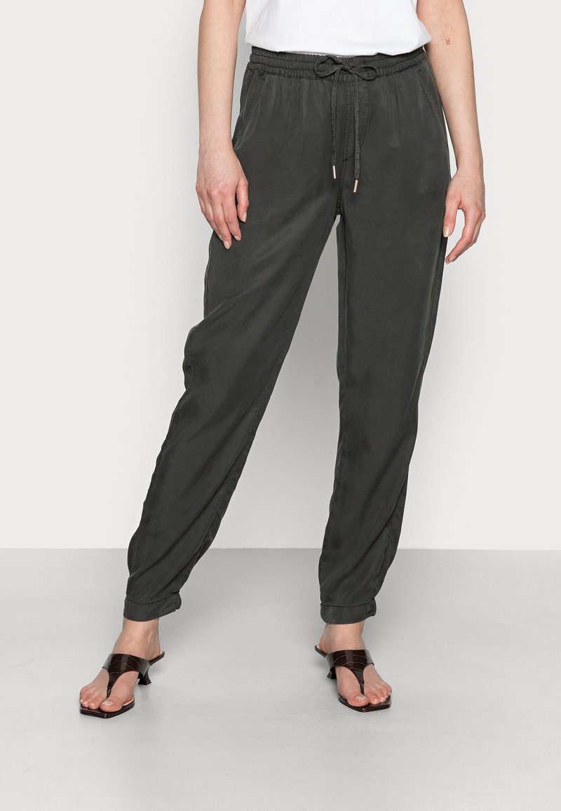 Pantalon gris foncé, léger et fuselé, avec une taille élastique et un cordon de serrage. Comprend des poches latérales et une texture douce. Porté avec des sandales marron.