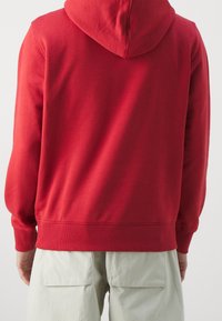 Sudadera de algodón roja con bolsillo canguro, puños y dobladillo acanalados. La tela tiene una textura suave y presenta un acabado sólido y liso.