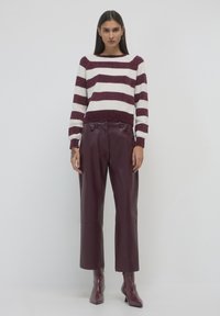 Gestreifter Strickpullover in Creme und Bordeaux mit gerippten Bündchen, kombiniert mit bordeauxfarbenen Kunstlederhosen und Stiefeletten.