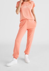 Koralowy zestaw z bawełnianej mieszanki do noszenia w domu, składający się z krótkiego T-shirtu z nadrukiem oraz dopasowanych spodni dresowych z elastycznym pasem i sznurkiem do regulacji.