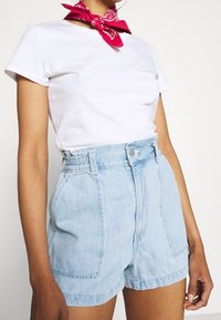 White t-shirt paired with light blue denim shorts featuring a high waist, front pockets, and a slight fray at the hem. Red bandana accessory.