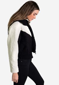 Chaqueta de felpa en blanco y negro con bloqueos de color, con un cuello alto, cierre de cremallera, puños acanalados y un diseño corto.