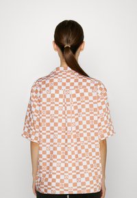 Short-sleeve shirt in light fabric with a repeating orange and white checker pattern. Features a collar and a straight cut.