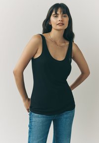 Sort ribbet tanktop med rund halsudskæring, kombineret med lyseblå denimjeans. Glat tekstur med en kropsnær pasform.