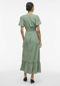 Zielona maxi sukienka z krótkimi puffowanymi rękawami, marszczonym pasem i falbaną u dołu. Wykonana z lekkiego materiału, charakteryzuje się gładką strukturą i zwiewnym fasonem.